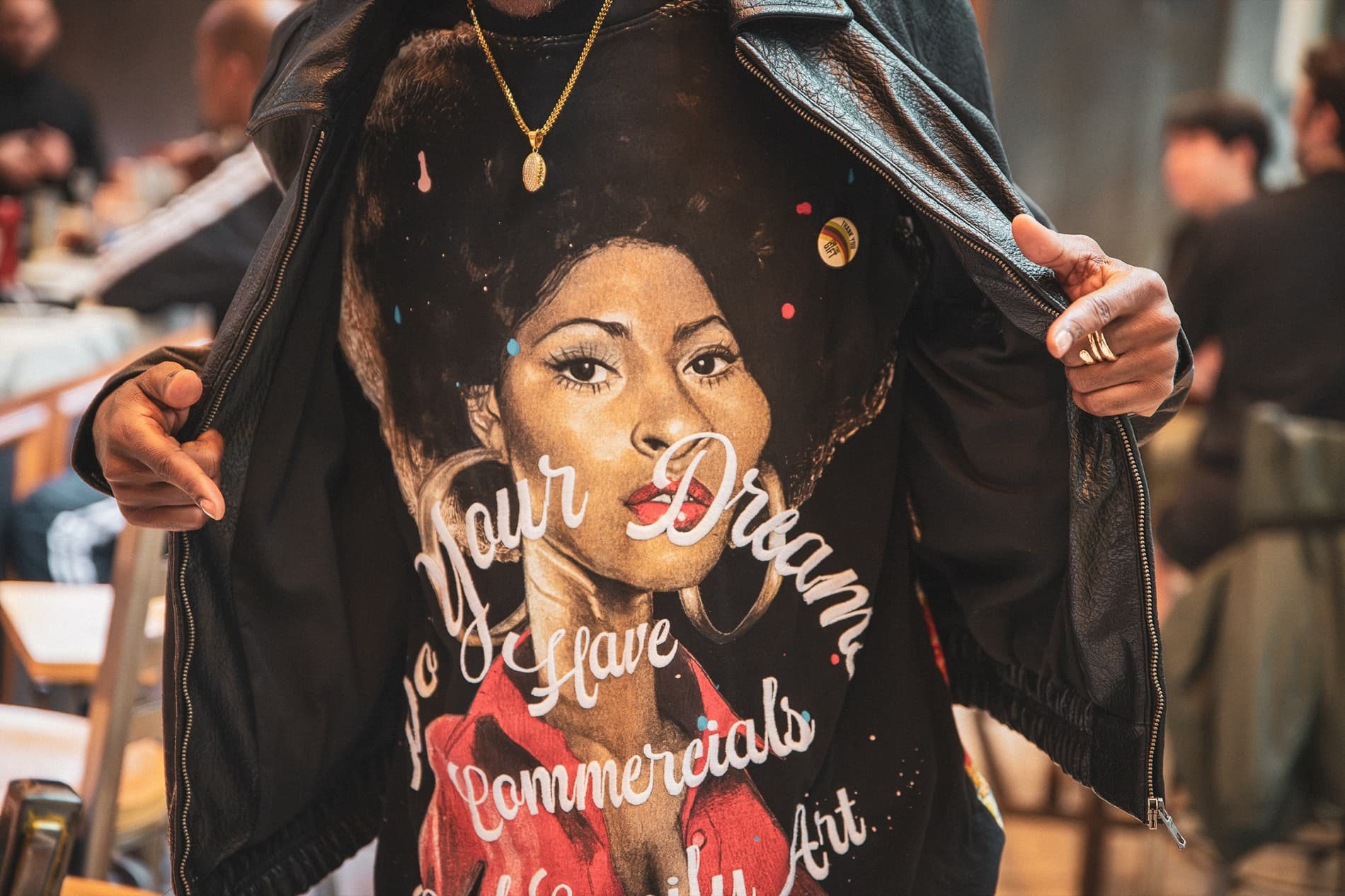 A man opens his leather jacket to show a T-shirt printed with a portrait of a woman and script lettering.