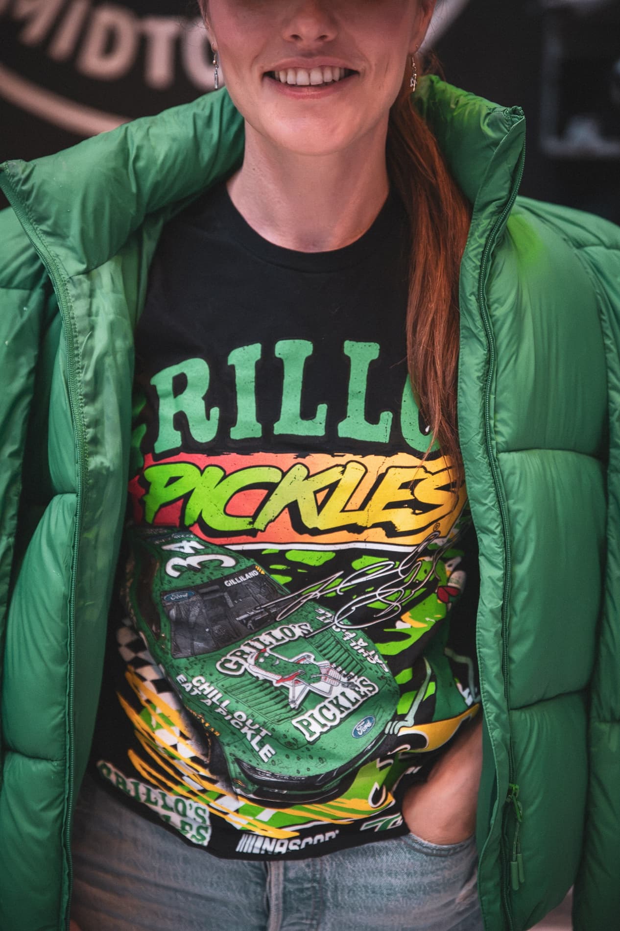 Close view of a black Grillo's Pickles race T-shirt worn under a green puffer jacket.