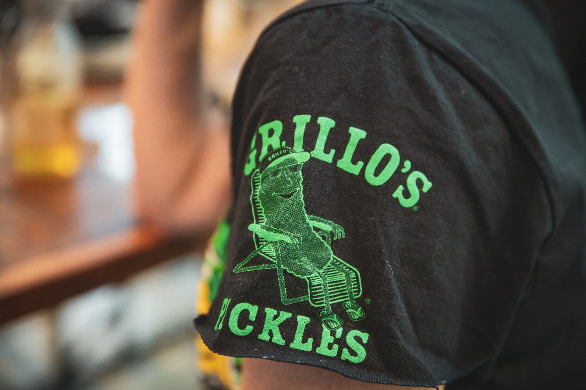 Close-up of a Grillo's Pickles logo printed on a T-shirt sleeve.