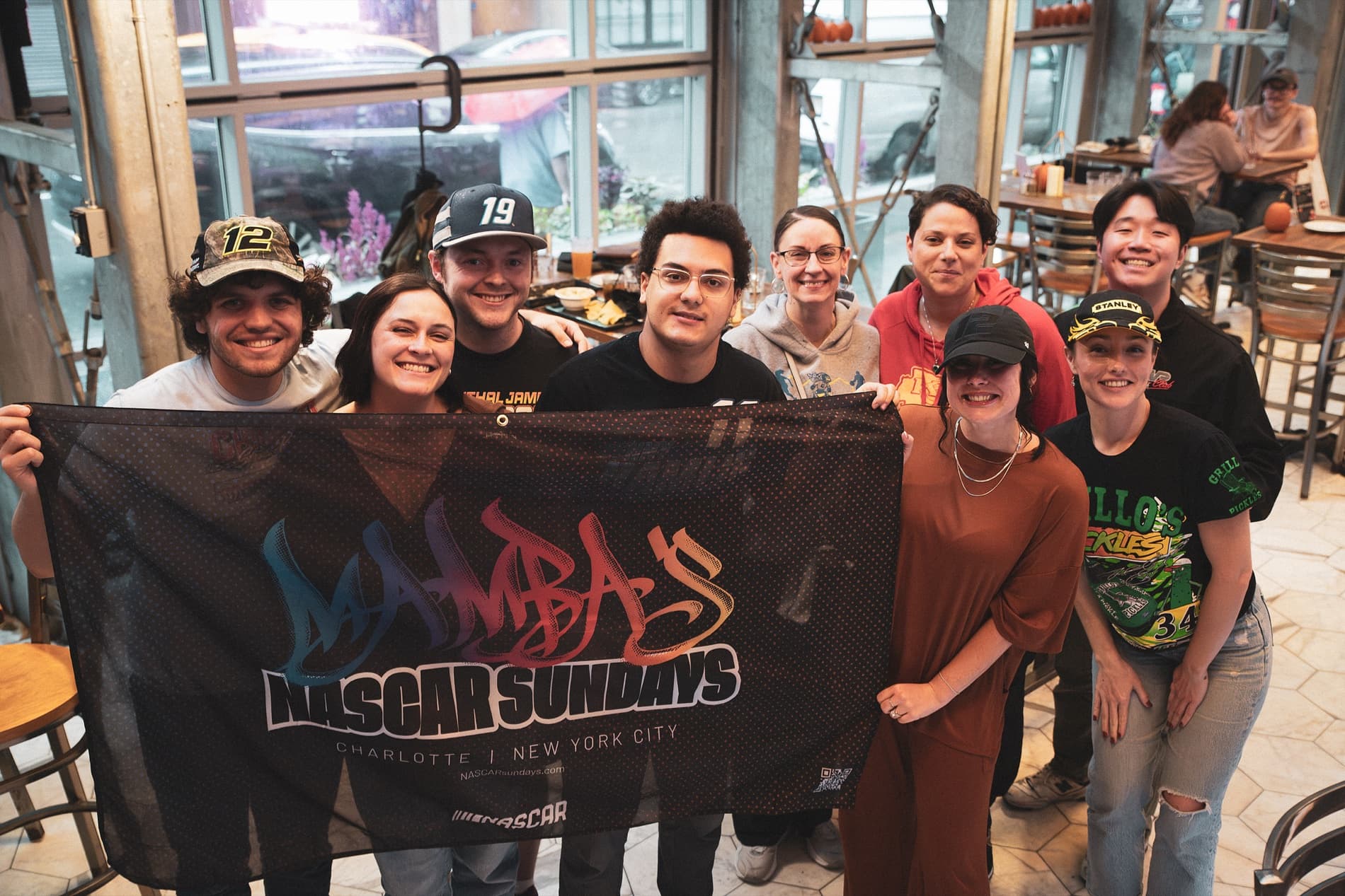 About a dozen fans hold up the Mamba's NASCAR Sundays banner inside Burgerology.