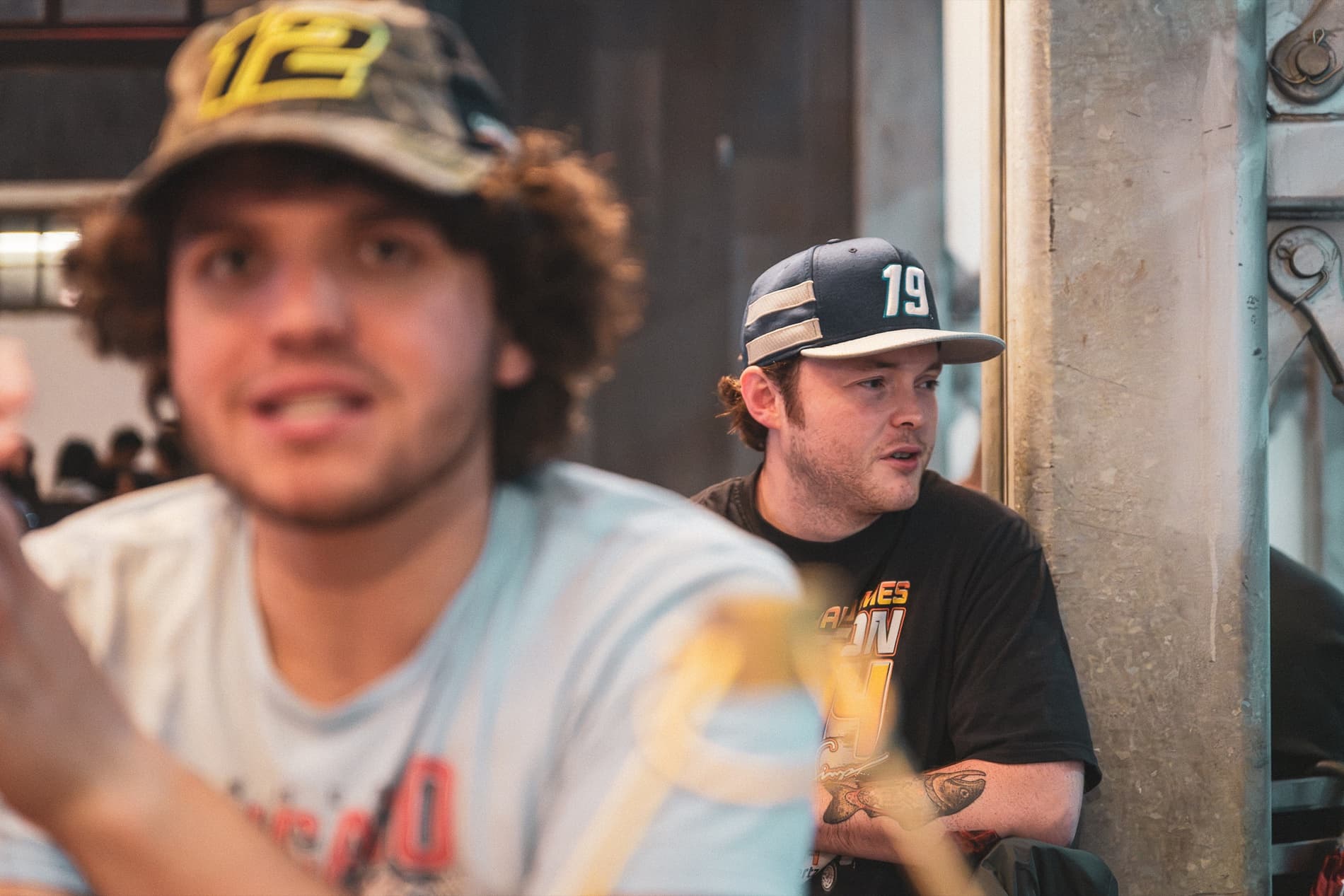 Two fans in No. 12 and No. 19 caps at a table, one mid-conversation.
