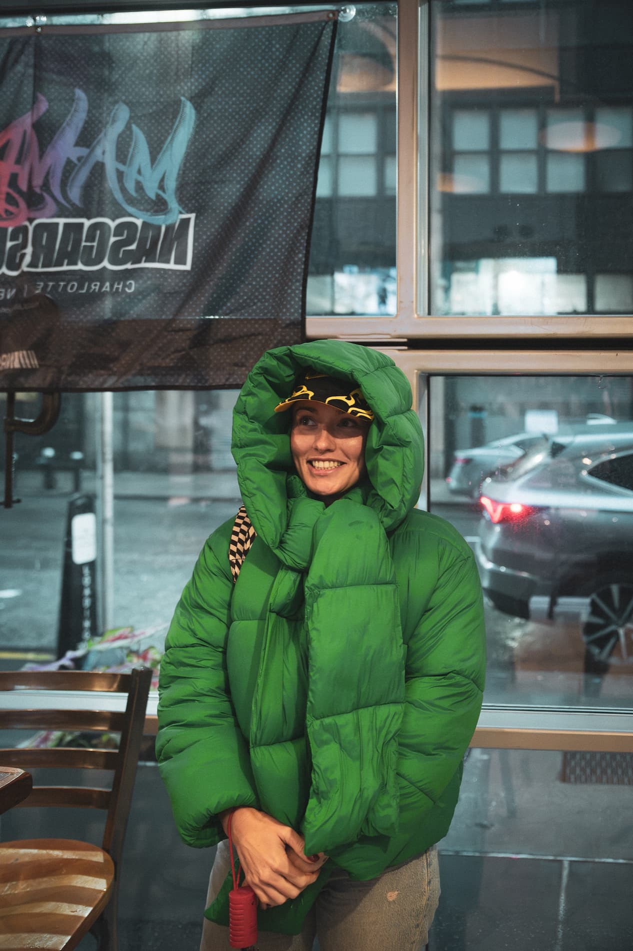 A woman bundled in a green puffer jacket with the hood up smiles beneath the NASCAR Sundays banner.
