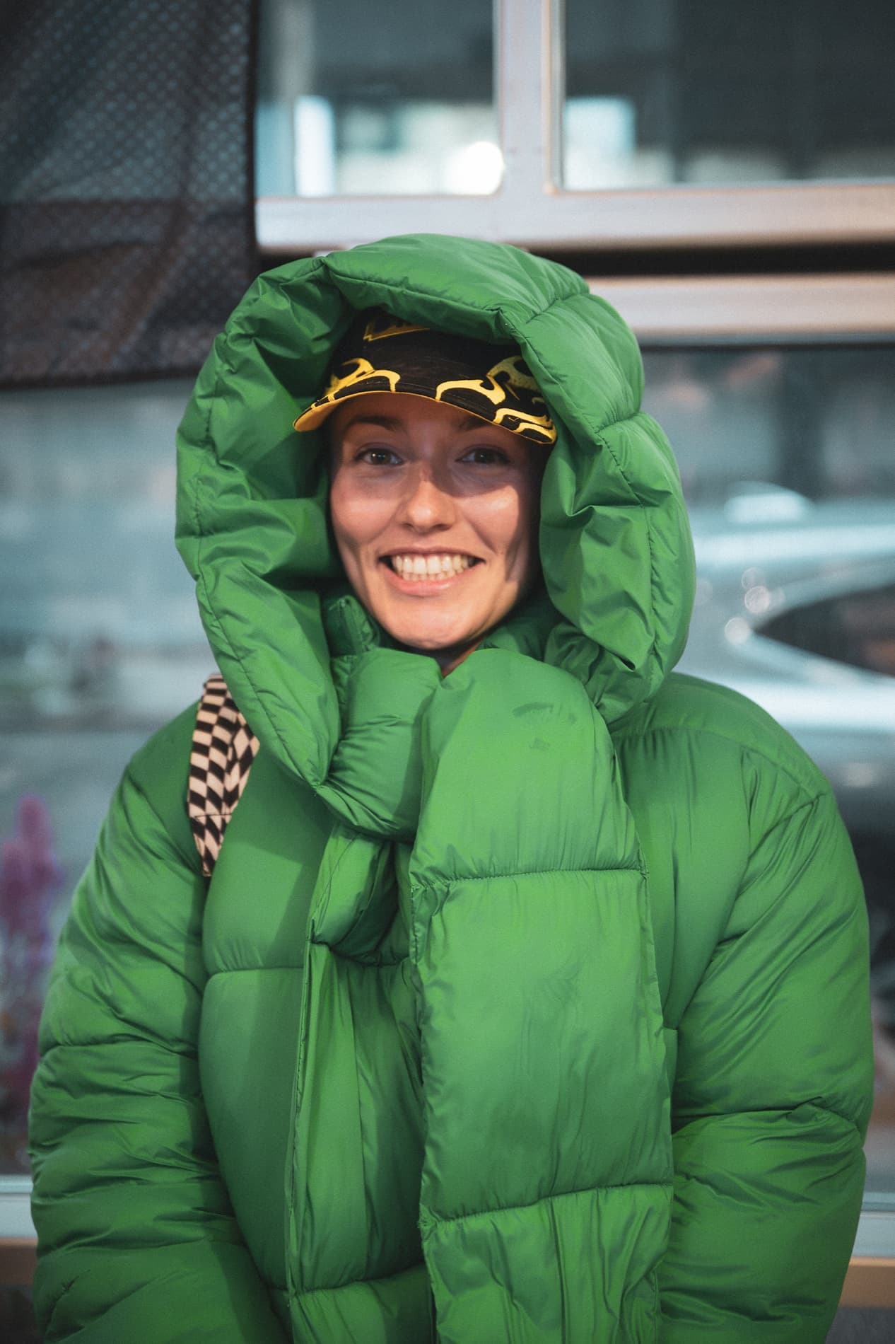 A woman in a hooded green puffer jacket and race cap grins at the camera.